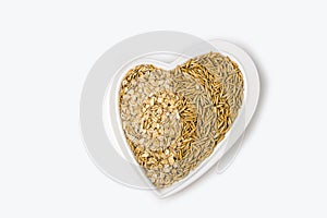 Oatmeal flakes and oats on a heart shaped plate on white background. Healthy breakfast. Organic and vegetarian food. Porridge and