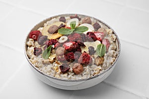 Oatmeal with freeze dried fruits, nuts and mint on white tiled table, closeup