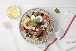 Oatmeal with freeze dried fruits, nuts and mint on white tiled table, flat lay