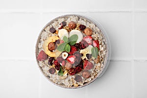 Oatmeal with freeze dried fruits, nuts and mint on white tiled table, top view