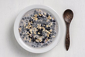 Oatmeal with fresh blueberry, almond milk and honey for breakfast in plate on wooden background. Rustic style. Top view