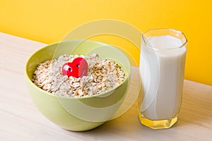 oatmeal in a green bowl with a red happy heart and a glass of milk on a wooden table