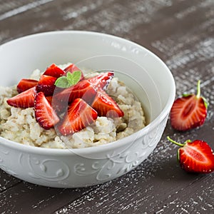 Oatmeal with honey and strawberries in a white bowl on a dark wooden table.