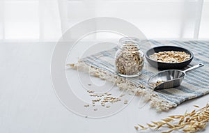 Oatmeal in a jar and in a bowl on a napkin on a white textured table in front of the kitchen window