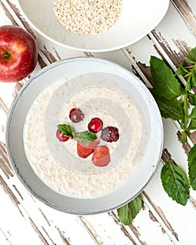 Oatmeal with milk and berries. Nutritious breakfast, wholesome healthy food. Bowl of porridge cereal oats with fresh red