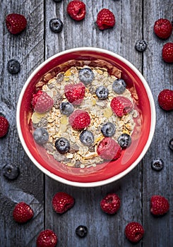 Oatmeal muesli with fresh berries in red bowl on blue rustic backgrund, top view. Sport, health and diet food concept. photo