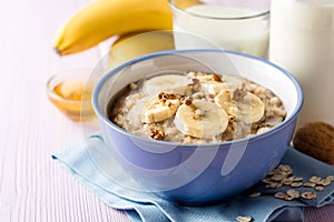 Oatmeal porridge with banana, walnuts and honey in bowl on purple wooden background. Healthy breakfast.