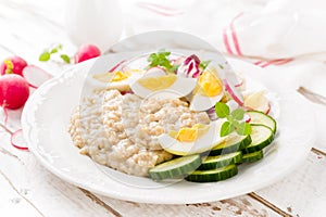 Oatmeal porridge with boiled egg and vegetable salad with fresh radish, cucumber and lettuce. Healthy dietary breakfast