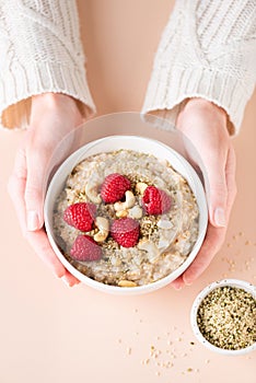 Oatmeal porridge bowl with berries and nuts in woman`s hands