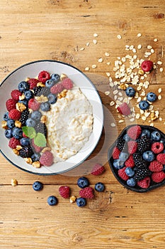 Oatmeal porridge in bowl with blueberry, nuts and raspberry on wooden table from above. Tasty and diet breakfast