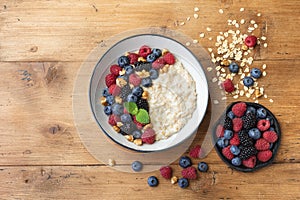 Oatmeal porridge in bowl with blueberry, nuts and raspberry on wooden table top view. Yummy and diet breakfast