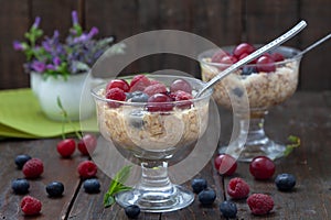 Oatmeal porridge with fresh blueberries, raspberries and cherries in glass bowl on wooden table