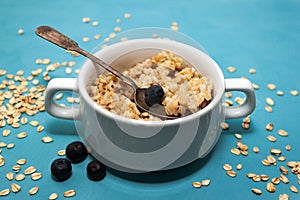 Oatmeal porridge with fresh blueberries in white bowl on blue background, linen napkin, silver spoon