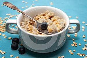 Oatmeal porridge with fresh blueberries in white bowl on blue background, linen napkin, silver spoon