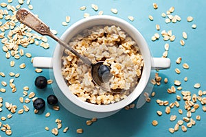 Oatmeal porridge with fresh blueberries in white bowl on blue background, linen napkin, silver spoon