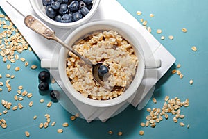 Oatmeal porridge with fresh blueberries in white bowl on blue background, linen napkin, silver spoon