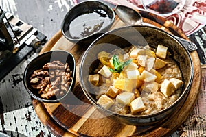 Oatmeal porridge with pieces of fruit, nuts and honey in bowl on wooden background. Healthy breakfast, top view