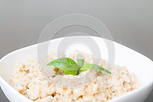 Oatmeal porridge / porridge oats / breakfast cereals decorated with green leafs on wooden table. Healthy eating, breakfast food