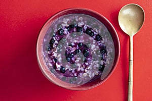 Oatmeal porridge with ripe blueberries for healthy breakfast on red background, closeup, top view