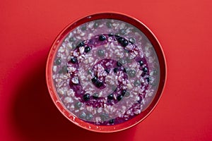 Oatmeal porridge with ripe blueberries for healthy breakfast on red background, closeup, top view