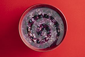 Oatmeal porridge with ripe blueberries for healthy breakfast on red background, closeup, top view