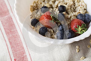 Oatmeal porridge with strawberry, blueberry, flax seeds on gray background
