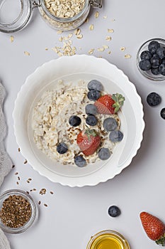 Oatmeal porridge with strawberry, blueberry, flax seeds and honey on gray background