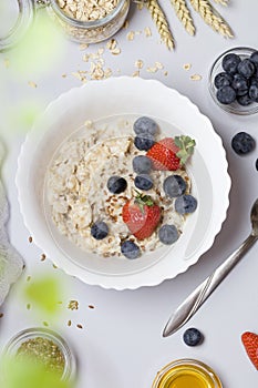 Oatmeal porridge with strawberry, blueberry, flax seeds and honey on gray background