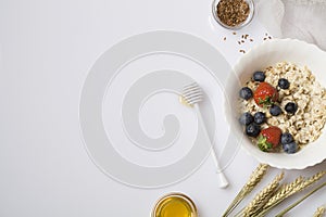 Oatmeal porridge with strawberry, blueberry, flax seeds and honey on white background