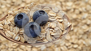 Oatmeal in spoon with blueberries. Oat flakes. Close-up rotating. Dry oat flakes grains background, rotation top view
