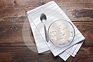 Oatmeal with spoon on cloth napkin on brown wooden background, top view