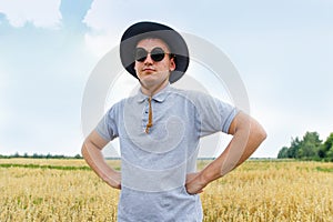 Oats plant. Harvester. Portrait of farmer standing in gold wheat field with blue sky in background. Young man wearing