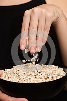 Oats Trickling from Hand into Bowl. Hand sprinkling rolled oats into a black bowl