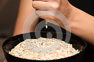 Oats Trickling from Hand into Bowl. Hand sprinkling rolled oats into a black bowl