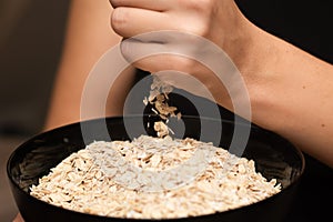 Oats Trickling from Hand into Bowl. Hand sprinkling rolled oats into a black bowl