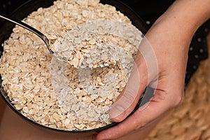 Oats Trickling from Hand into Bowl. Hand sprinkling rolled oats into a black bowl