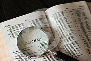 Obadiah prophet open Holy Bible Book with a magnifying glass on dark granite background