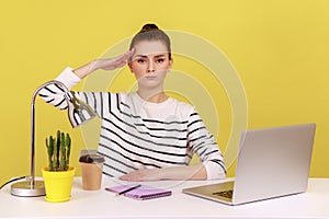 Obedient responsible woman office manager sitting at workplace with laptop and saluting.