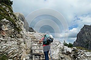 Oberbachernspitze - Woman with big backpack and sticks, walking up a wooden stairs in high Italian Dolomites.