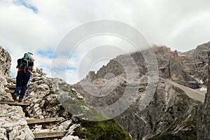 Oberbachernspitze - Woman with big backpack and sticks, walking up a wooden stairs in high Italian Dolomites.