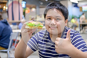 Obese boy enjoy to eating pork hamburger in a food court in a shopping center