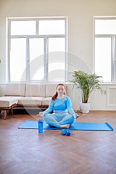 Obese chubby young female sitting on mat with eyes closed, meditating.