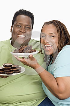 An Obese Couple Holding Plates Of Pastries