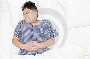 Obese fat boy suffering from stomachache and lying on bed