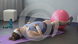 Obese girl trying to train lower body muscles raising big gym ball with her legs