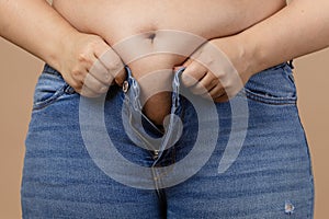 Obese lady with big abdomen trying to zip up jeans of blue colour. Visceral fat. Body positive. Sudden weight gain