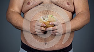 Obese male holding unhealthy hamburger in hands, overweight problem, cholesterol