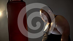 Obese man with aggression looking at punching bag imaging his opponent, box