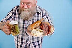 Obese man on blue background, focus on hands with plate of greasy food and beer