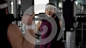 Obese man doing exercise with barbell in sport gym, desire to be strong and slim